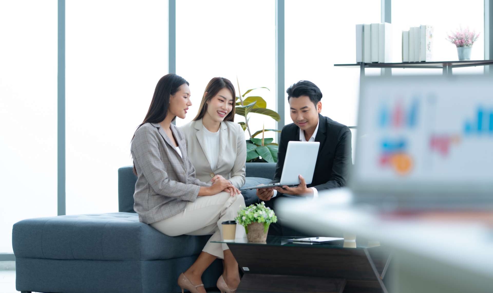 Two women and a man in corporate dress looking at a laptop screen